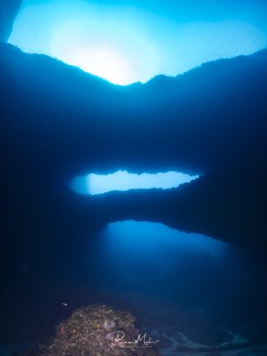 The Double Arch in Gozo in Xwejni Bay in backlight. The sun shines dramatically from above through the archways.