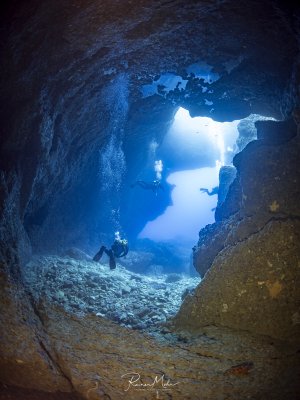Several divers swim out through the exit of the large cave behind the famous Blue Hole on Gozo. Air bubbles have collected on the cave ceiling and form a mirroring surface.