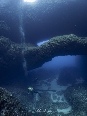 The Double Arch in Gozo in Xwejni Bay. A diver explores the impressive underwater landscape while sunlight from above mystically illuminates the scene.